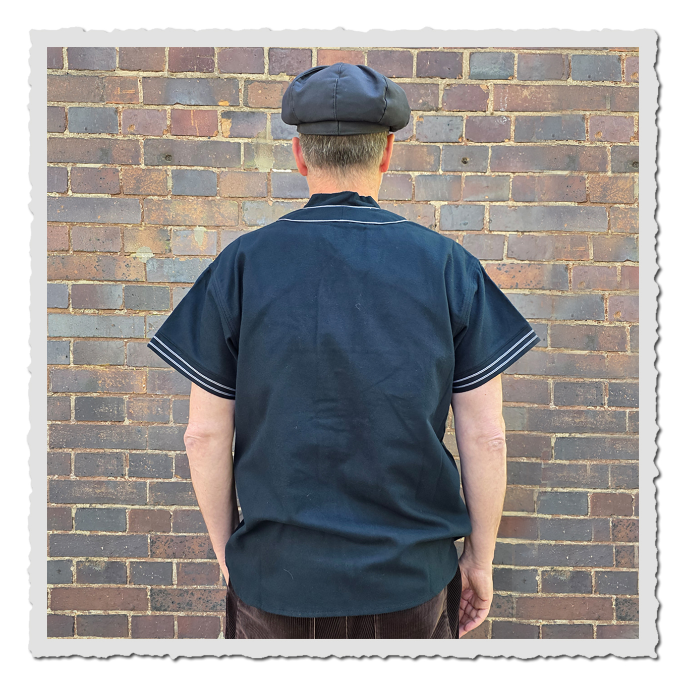 Rückansicht einer Person im dunkelblauen Baseballshirt vor Backsteinwand im Außenbereich.